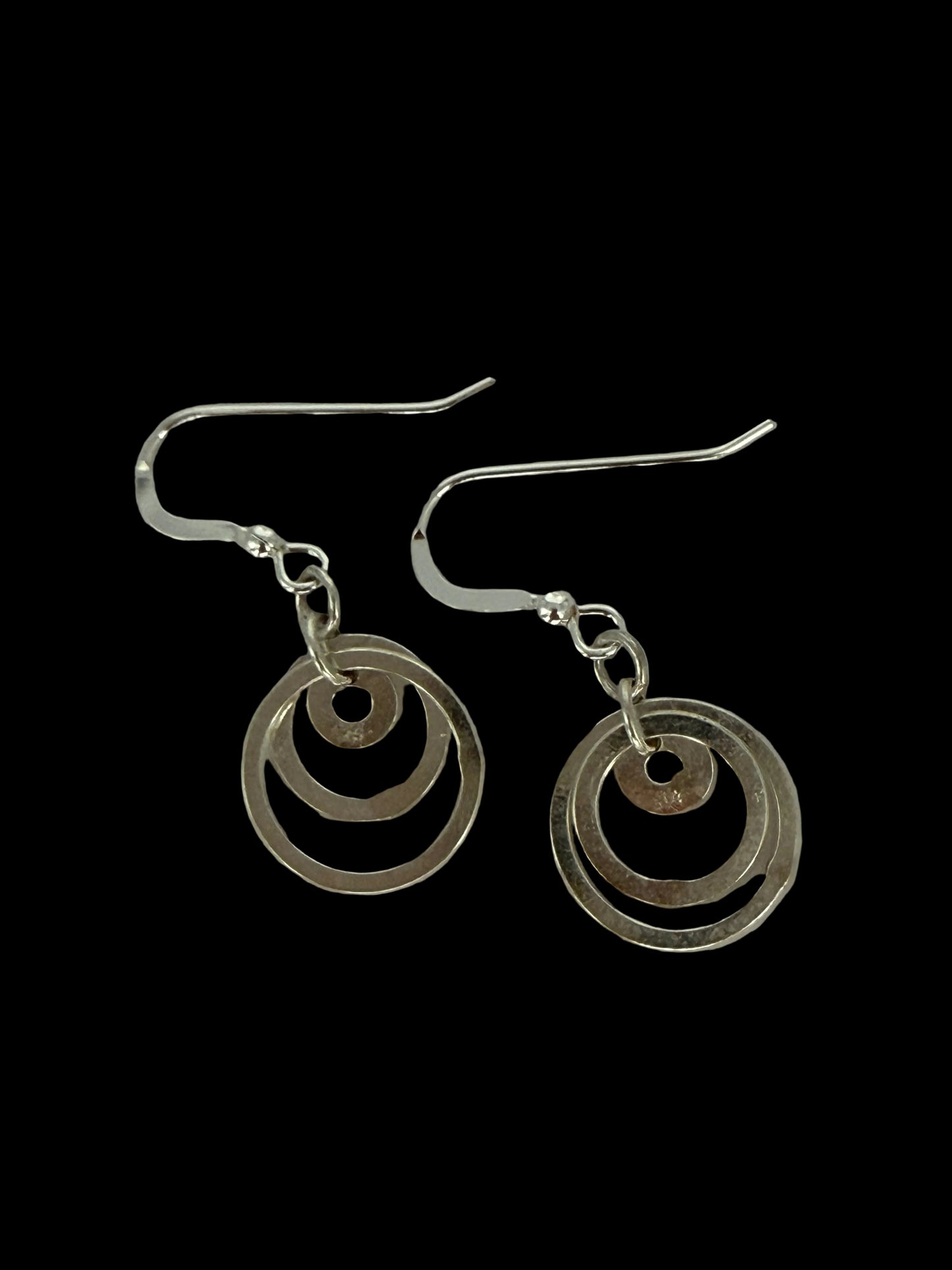 A pair of sterling silver dangle earrings featuring concentric circular cutouts, suspended from classic fishhook wires on a neutral light gray background.