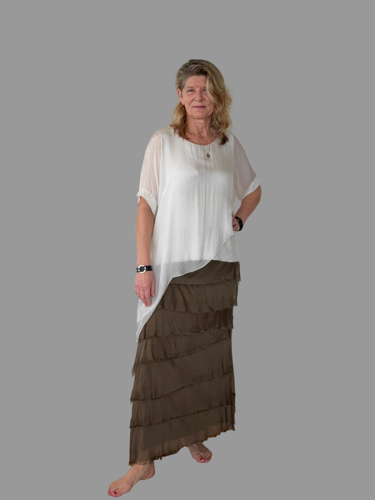 A woman modeling a two-piece outfit consisting of a white short-sleeve top and a brown tiered maxi skirt, set against a solid gray background.