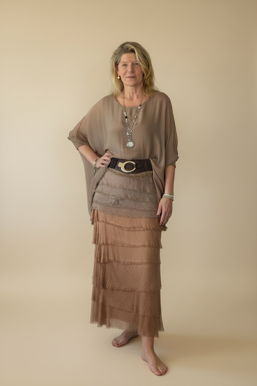 A woman modeling a two-piece taupe set consisting of a loose short-sleeve top and a tiered maxi skirt, styled with a wide black belt featuring a gold oval buckle.  Cheeky Goddess.  Australia.  Silk top and silk skirt.