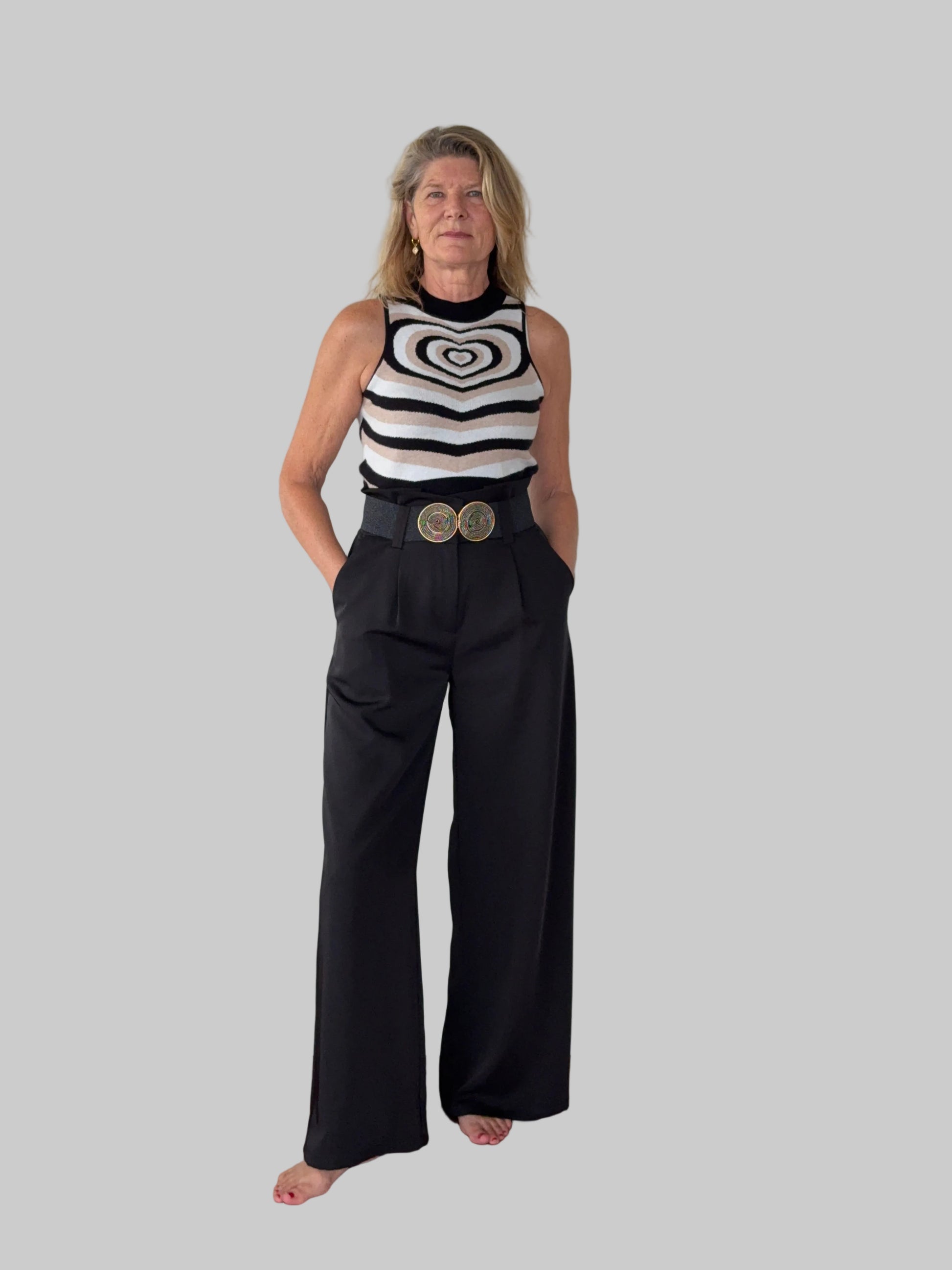Person wearing a sleeveless top with circular patterns and black pants on a white floor.