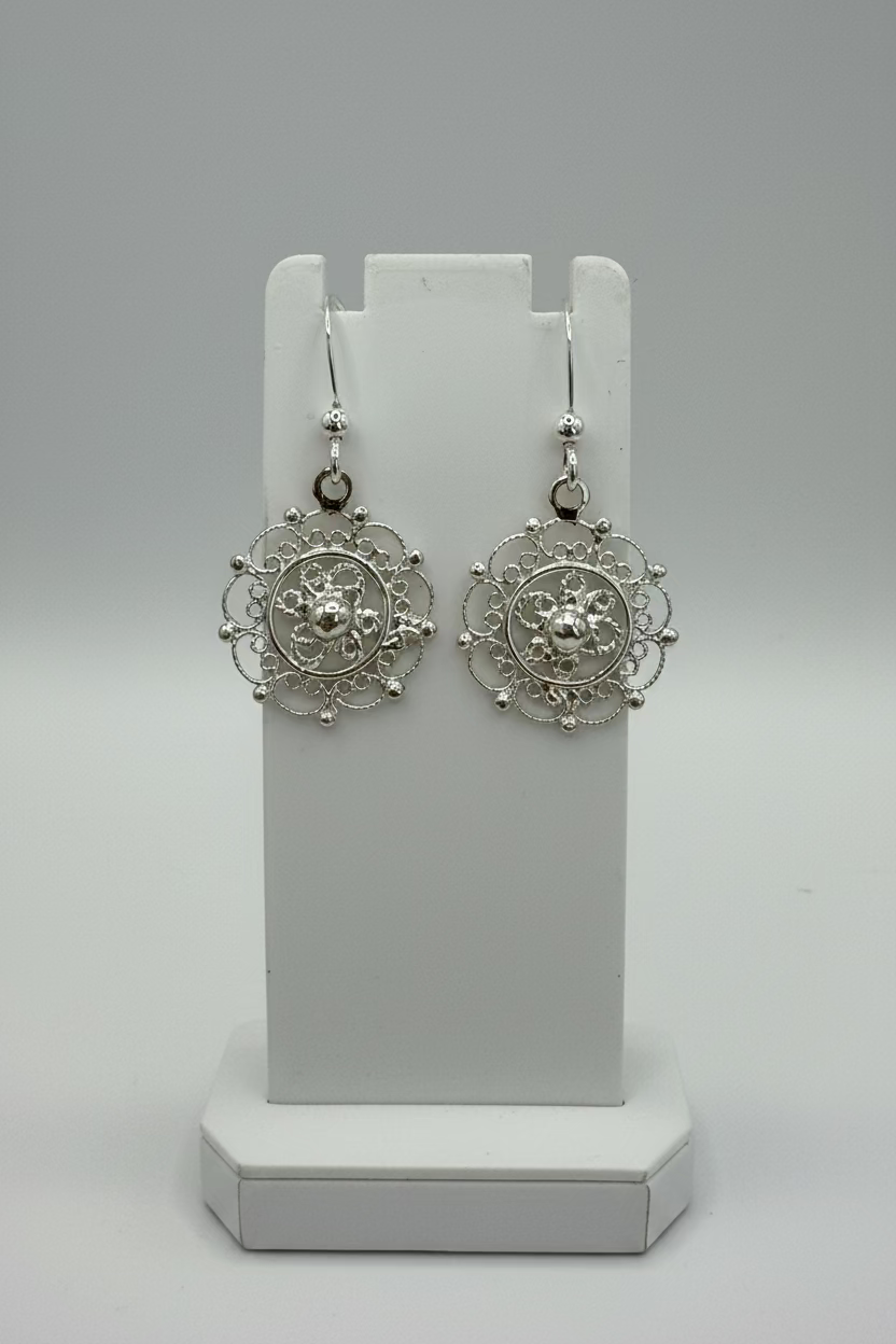 Pair of sterling silver filigree circle earrings on a white stand with a grey backgroun