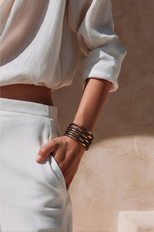 Person wearing a white outfit with hand in pocket with a brown magnetic bracelet with gold accents on her left wrist . beige background. cheeky goddess