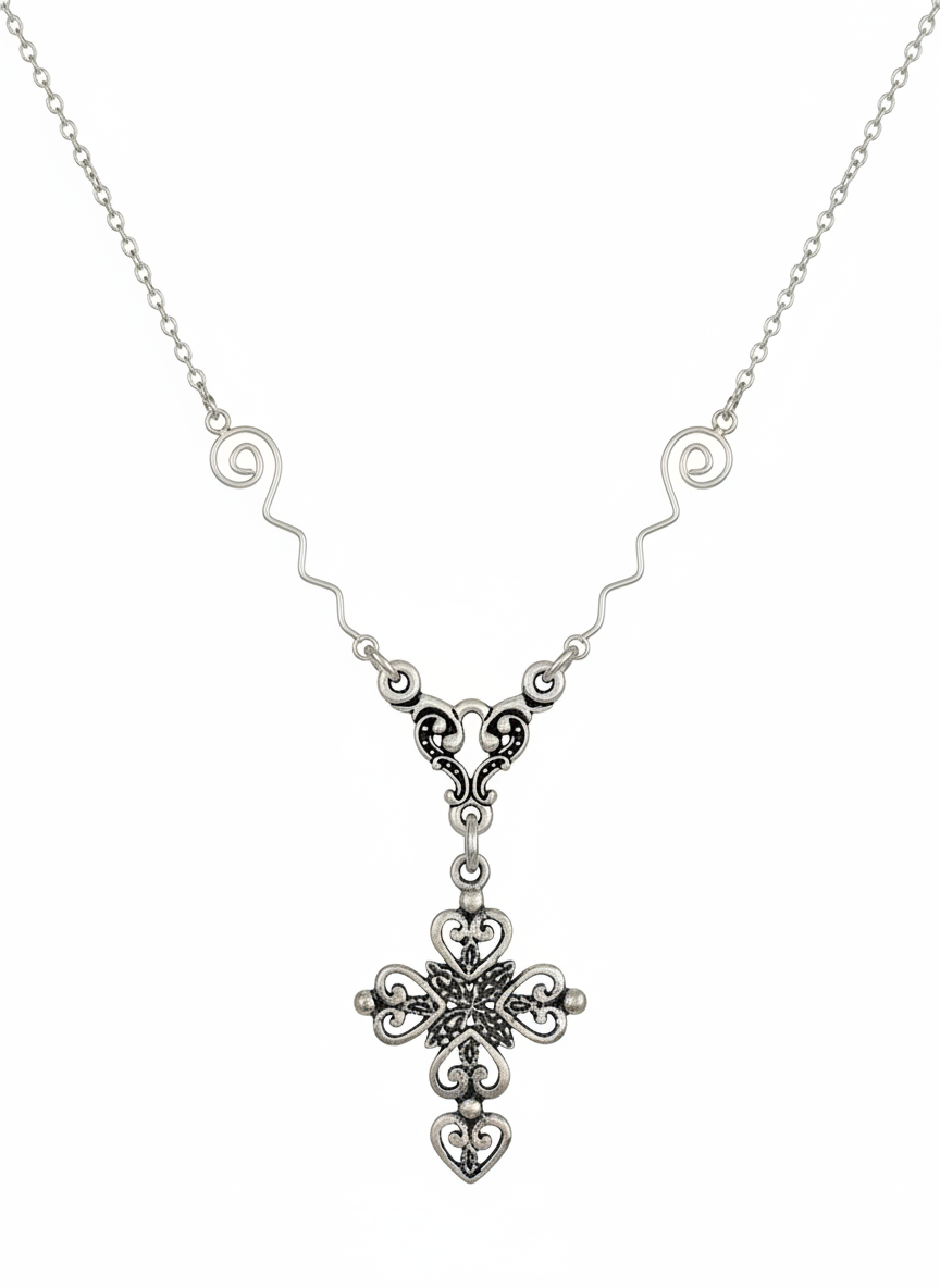A sterling silver necklace featuring a delicate chain, wavy side details, and an ornate filigree cross pendant with a small heart at the bottom, shown against a plain white background. Sterling silver.  Cheeky Goddess.