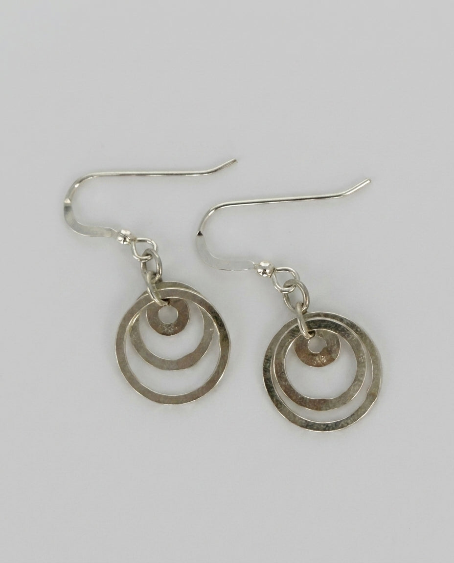 Drop Earrings — Macro Texture Detail | Generated by Modelize. fishhook air wires with three circle charms laying on a white background. All sterling silver Cheeky goddess