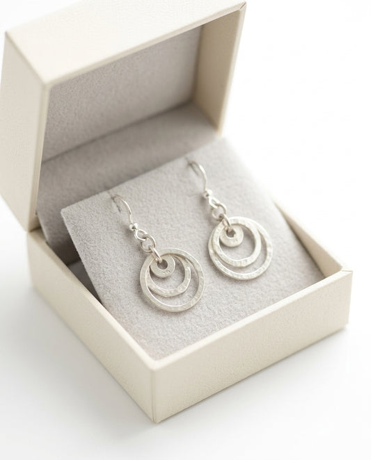 Sterling Silver earrings with fishhook ear wires charm has three Circles . Earrings are shown in a box cheeky goddess 
Drop Earrings — Gift Packaging | Generated by Modelize