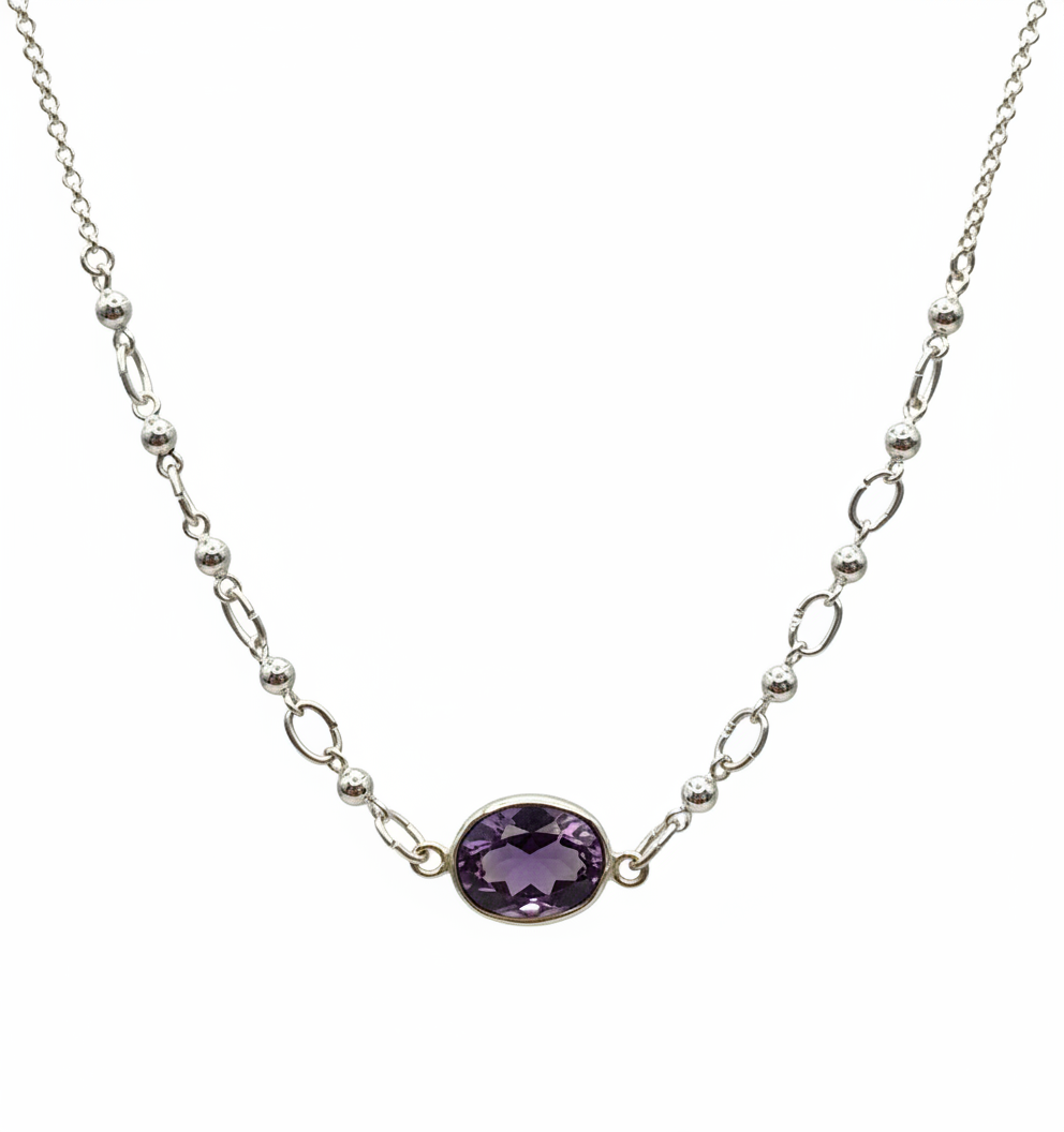 A silver-toned chain necklace featuring a central oval-cut purple gemstone pendant, displayed against a solid white background.