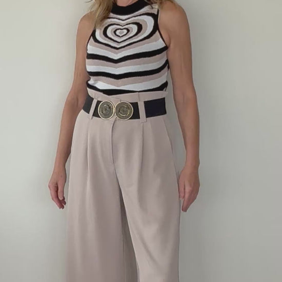 video of woman showing beige paperbag wide leg pants with black belt and geometric print heart knit tank top.  Cheeky Goddess - Australia - size 14