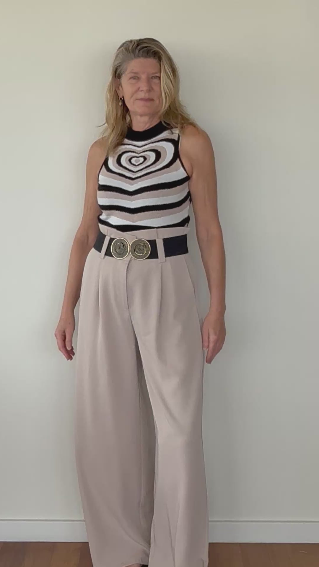 video of woman showing beige paperbag wide leg pants with black belt and geometric print heart knit tank top.  Cheeky Goddess - Australia - size 14